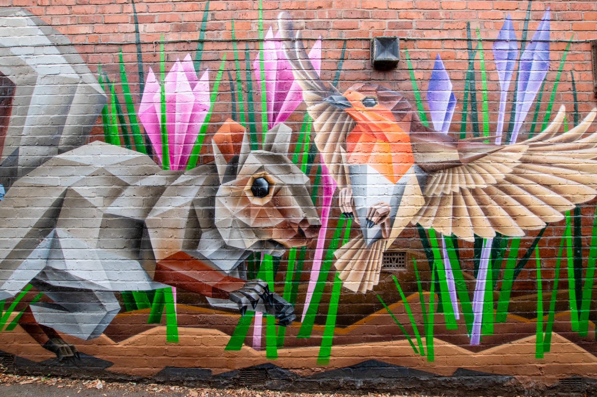 a mural on a brick wall by Annatomix featuring a squirrel, flowers, and a European robin in flight