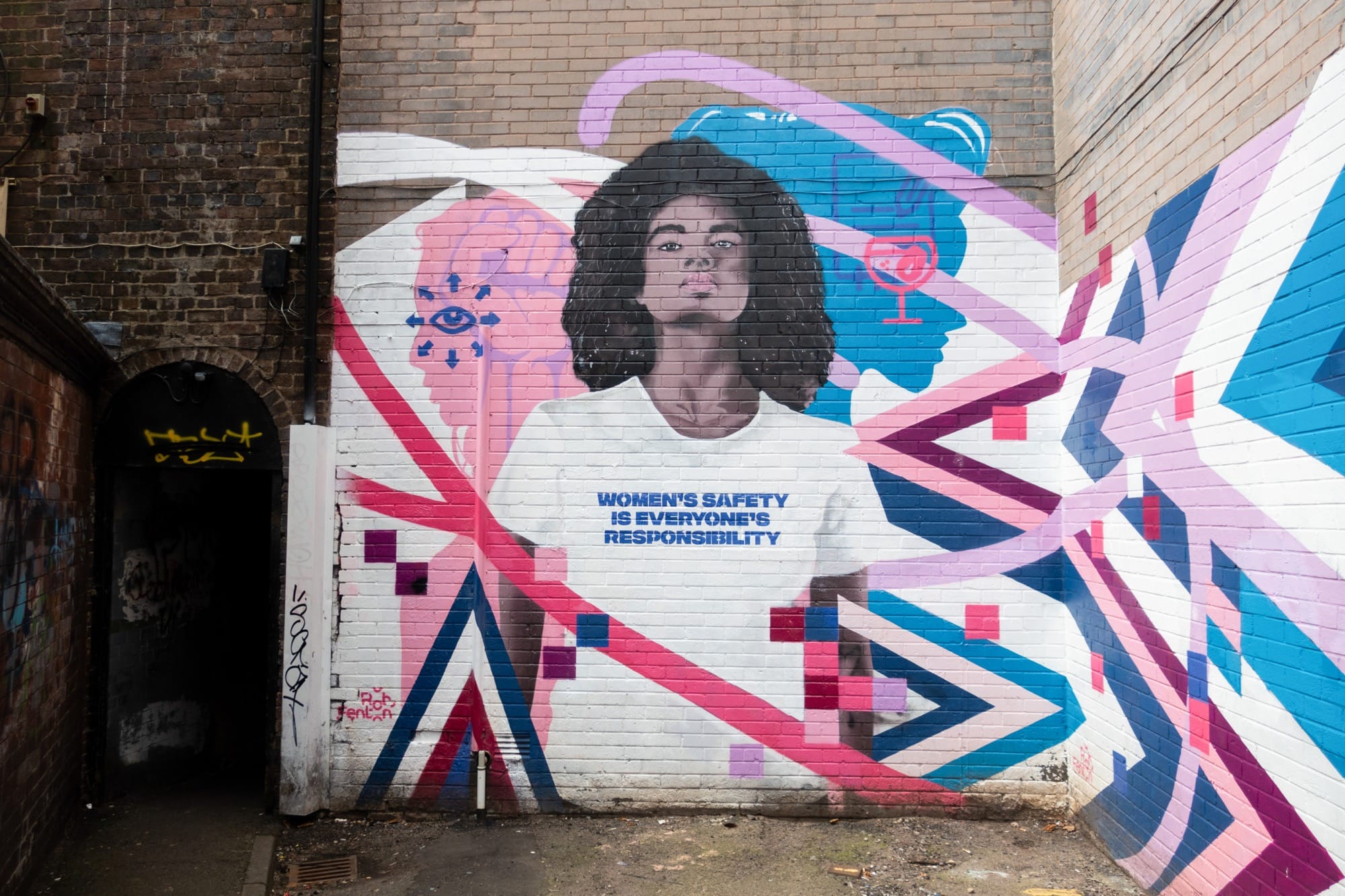 a mural by Rob Fenton featuring a young Black woman with a t-shirt that reads "women's safety is everyone's responsibility," surrounded by colorful graphics
