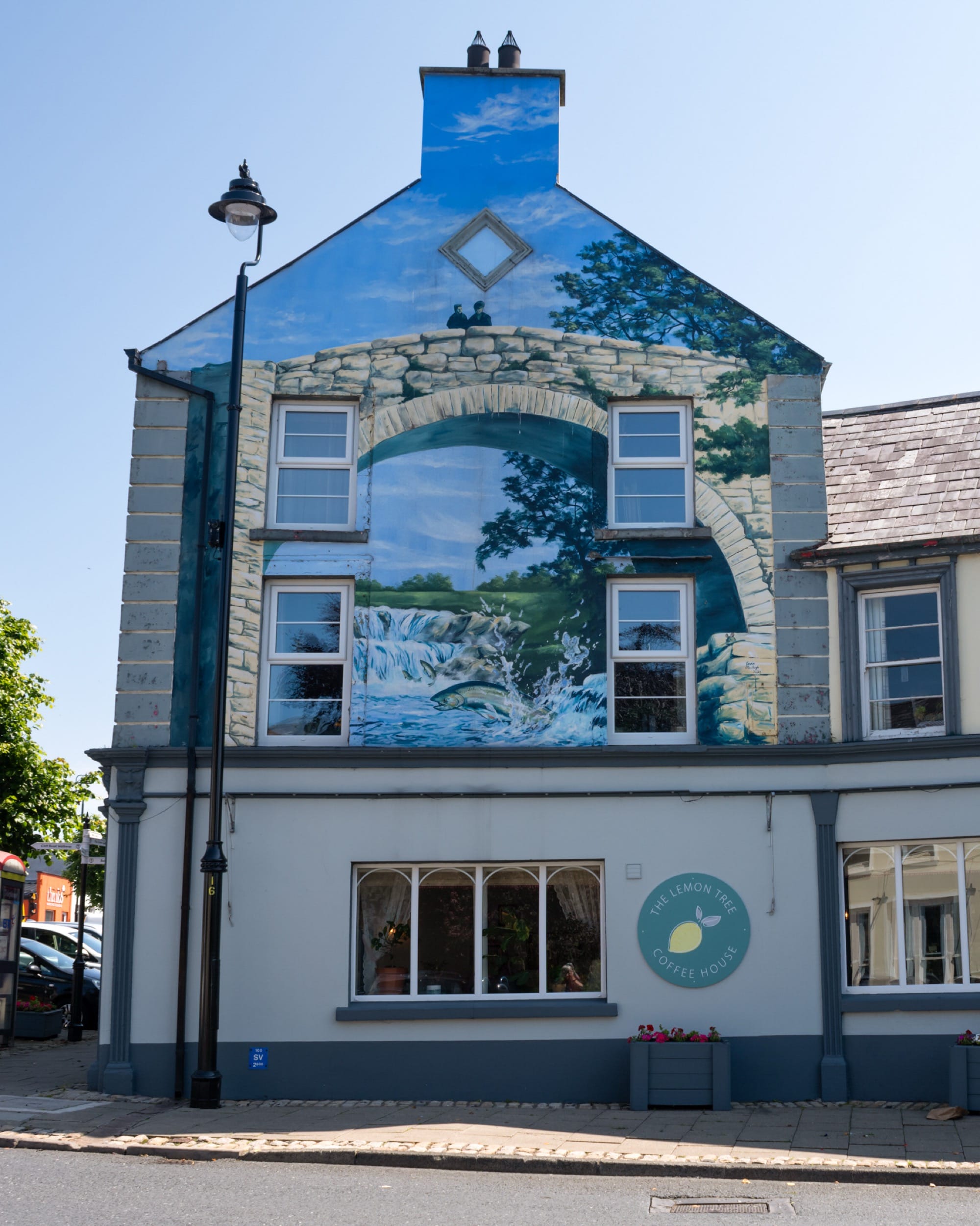 a mural on the end of a building featuring a trompe-l'oeil scene of crumbling architecture against a blue sky