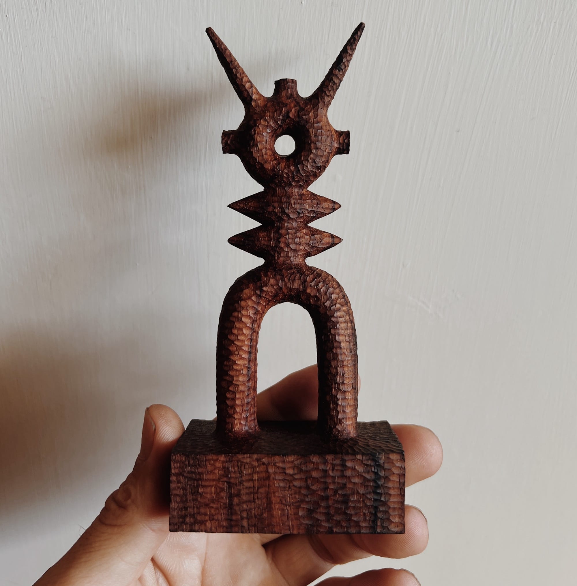 a hand holds up a small, abstract, spindly wooden sculpture