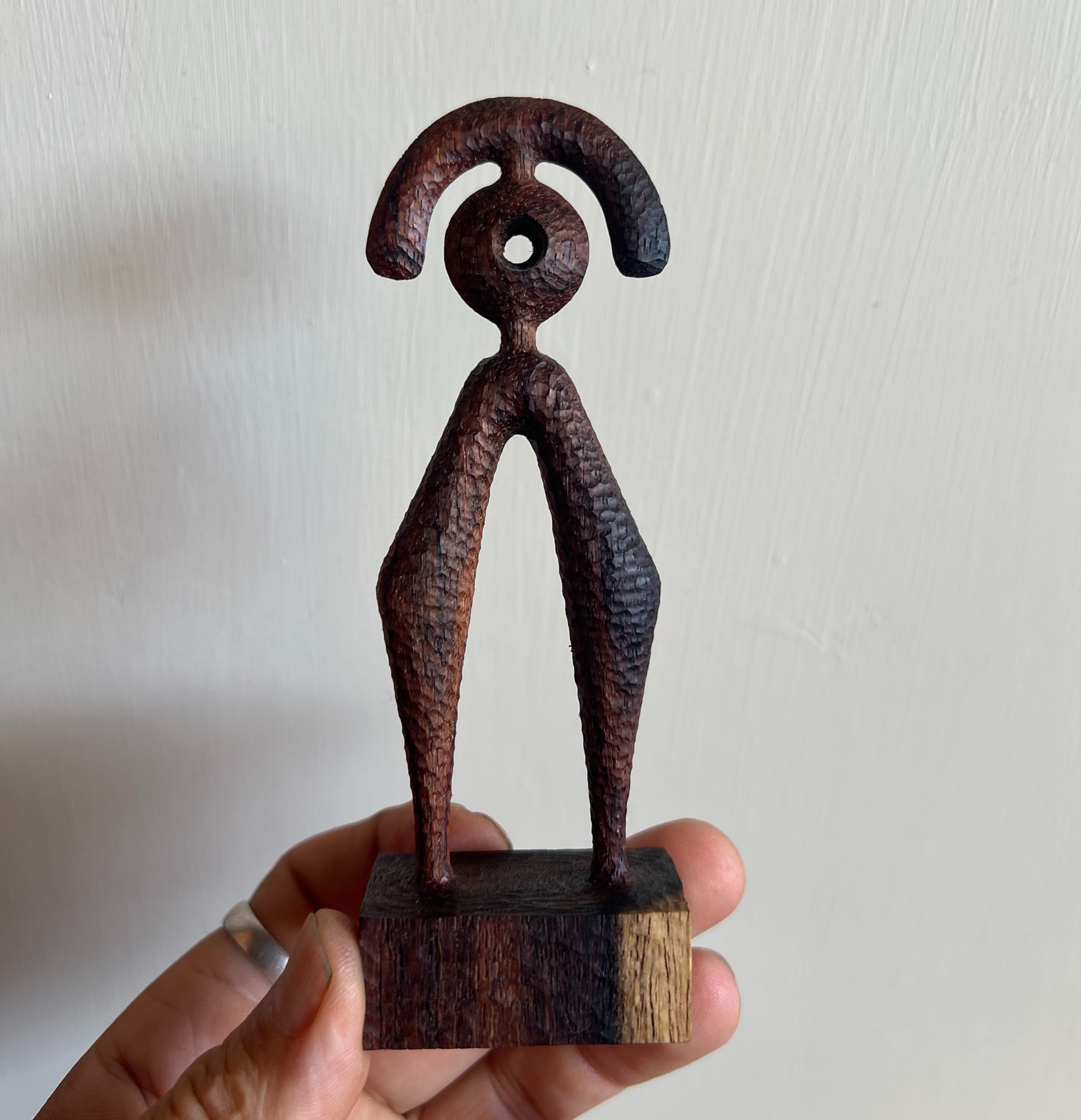 a hand holds up a small, abstract, spindly wooden sculpture