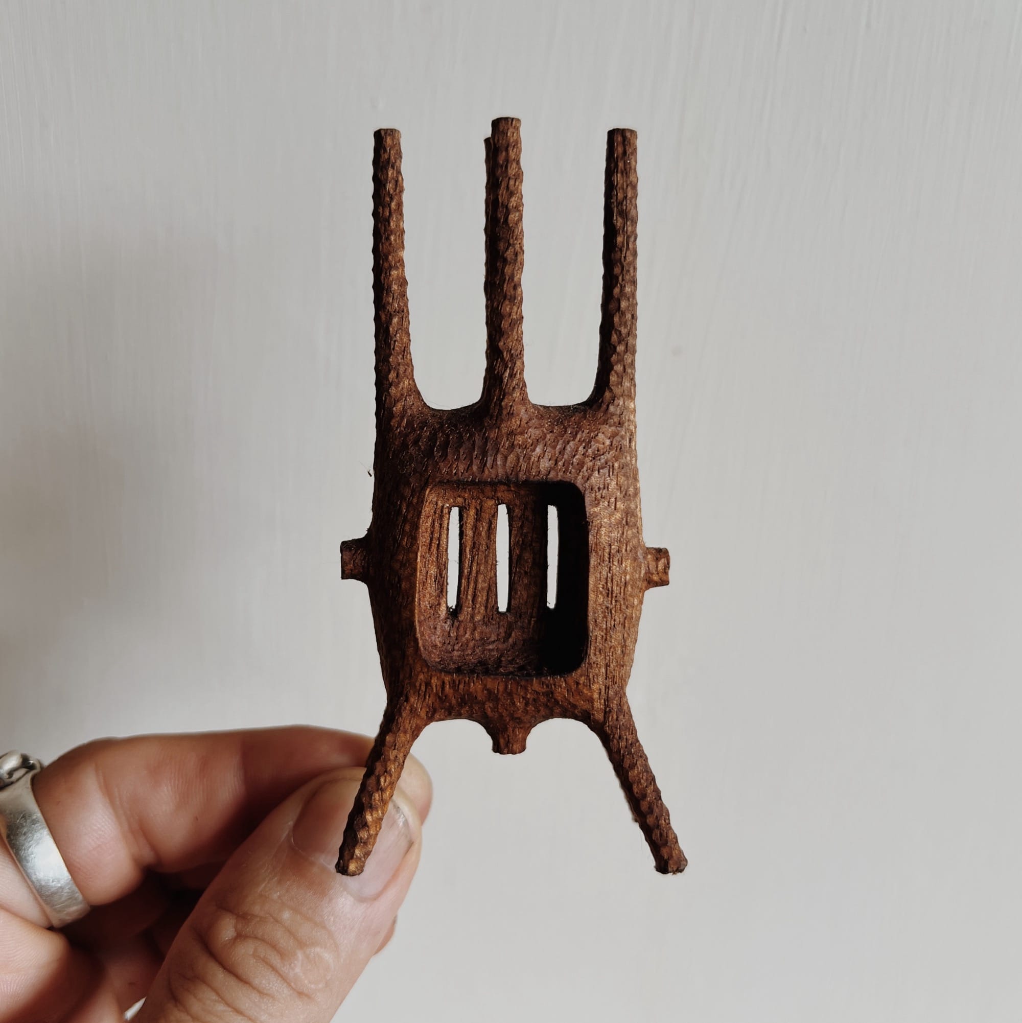 a hand holds up a small, abstract, spindly wooden sculpture