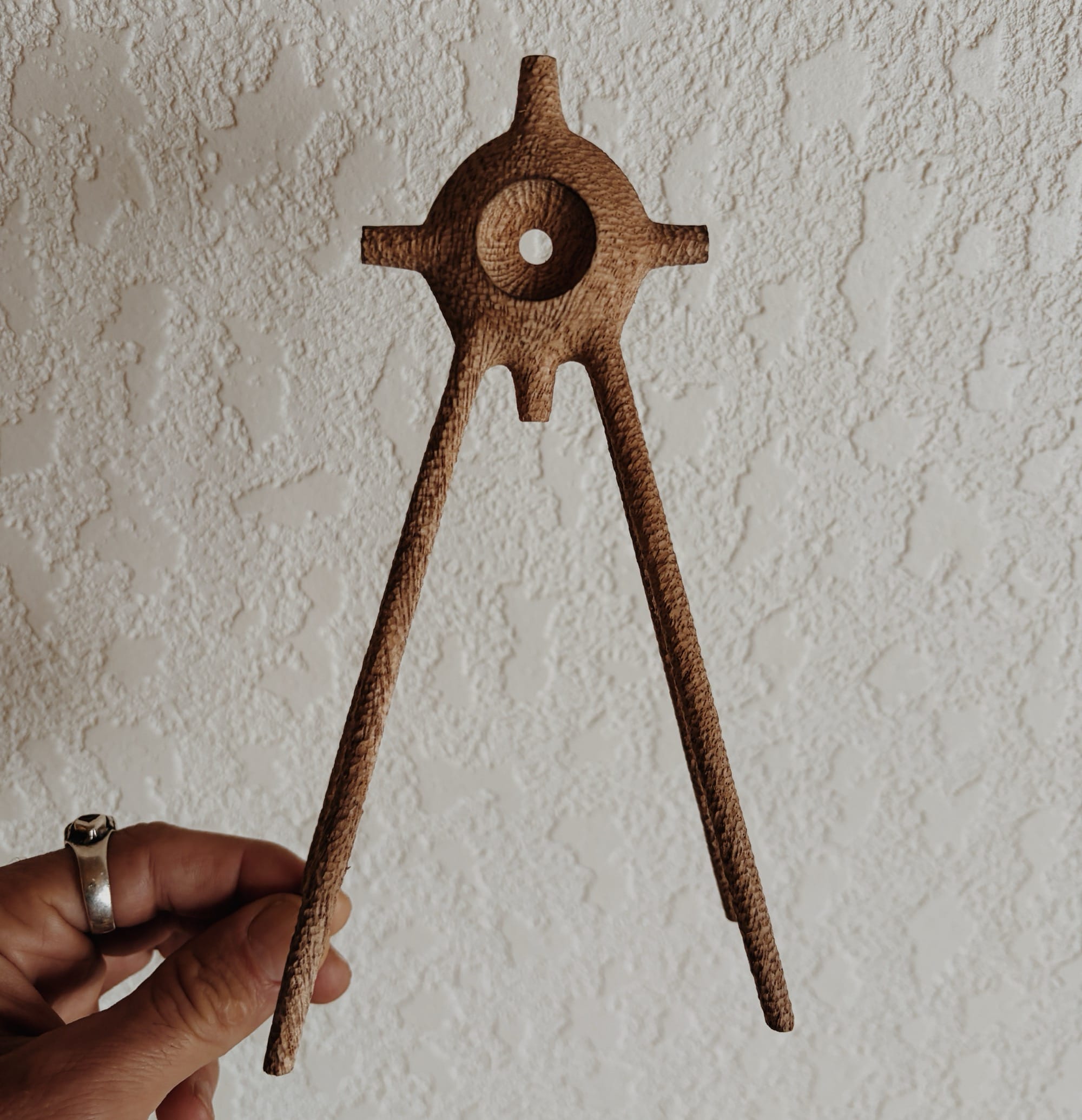 a hand holds up a small, abstract, spindly wooden sculpture