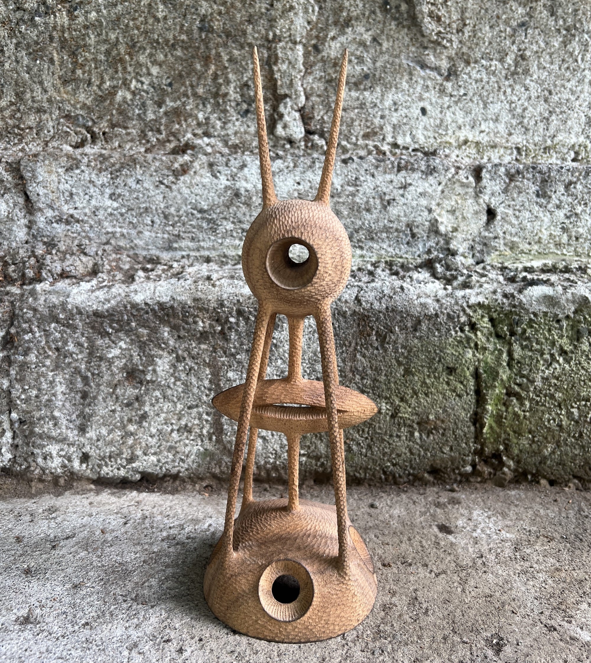 an abstract, spindly wooden sculpture against a concrete background