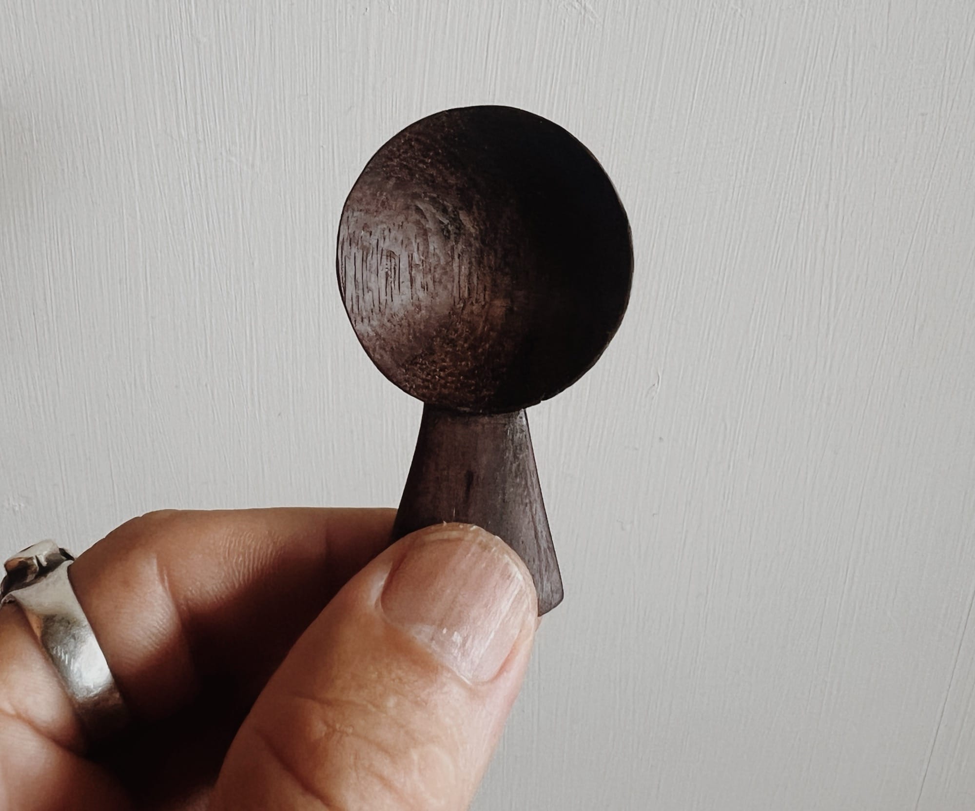 a hand holds up a small, abstract, wooden sculpture