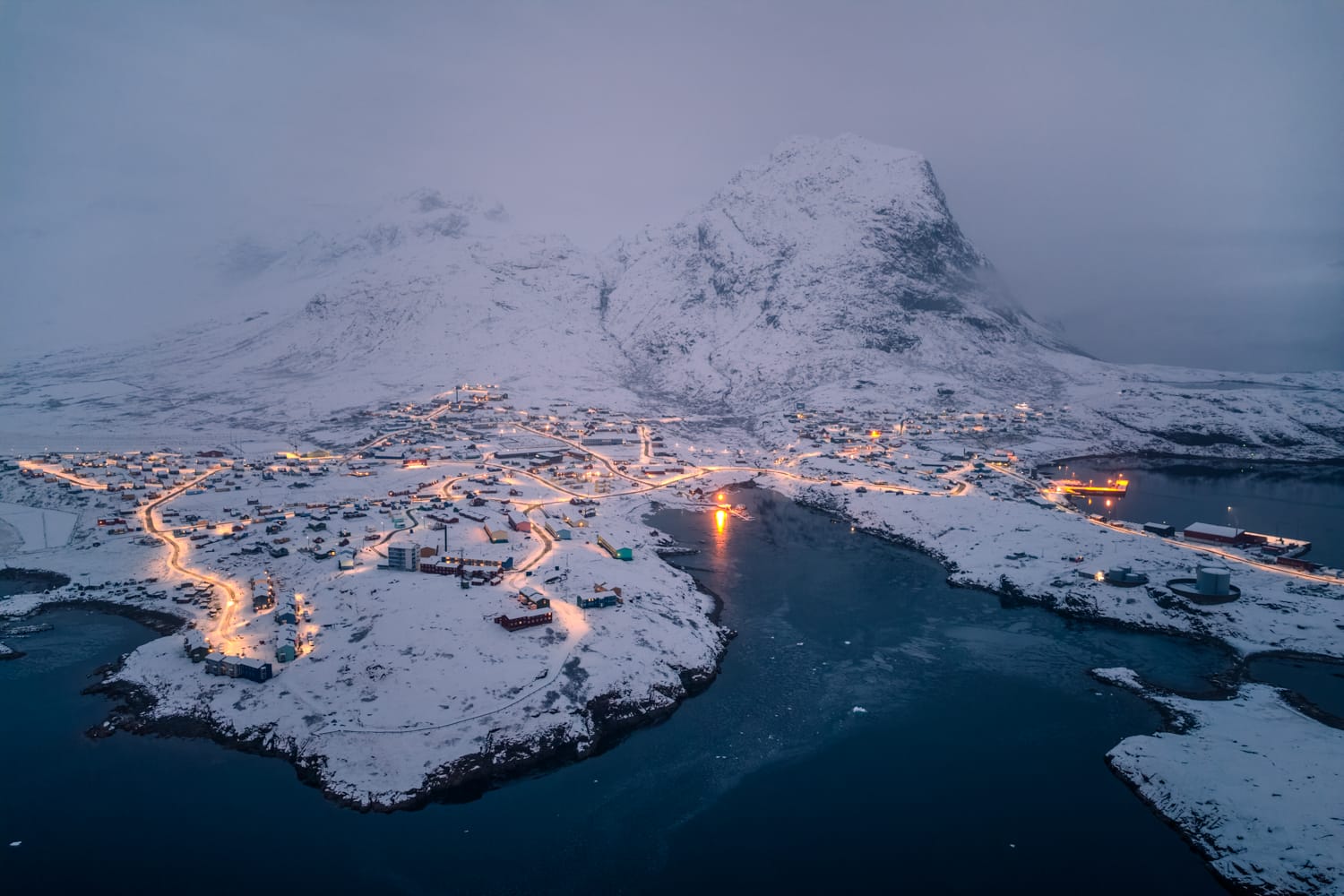 An aerial photograph of a small village called Narsaq in Greenland, situated at the base of snowy mountains